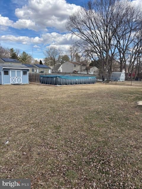 view of yard featuring a covered pool, an outdoor structure, fence, and a shed