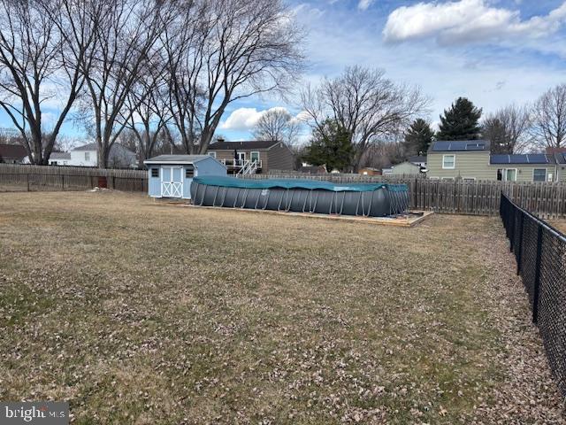 view of yard with an outbuilding, a storage unit, a fenced backyard, and a fenced in pool