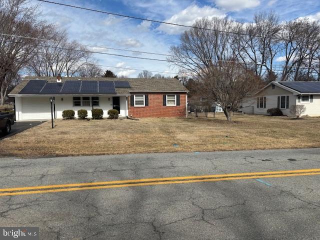 ranch-style house featuring a garage, solar panels, brick siding, driveway, and a front lawn