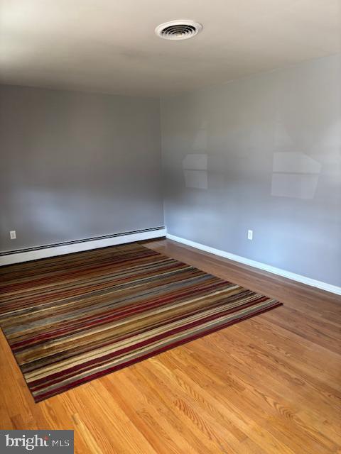 spare room with baseboard heating, wood finished floors, visible vents, and baseboards