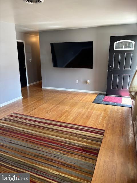 unfurnished living room featuring visible vents, baseboards, and wood finished floors