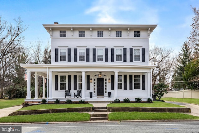 italianate home with covered porch, fence, a chimney, and a front lawn