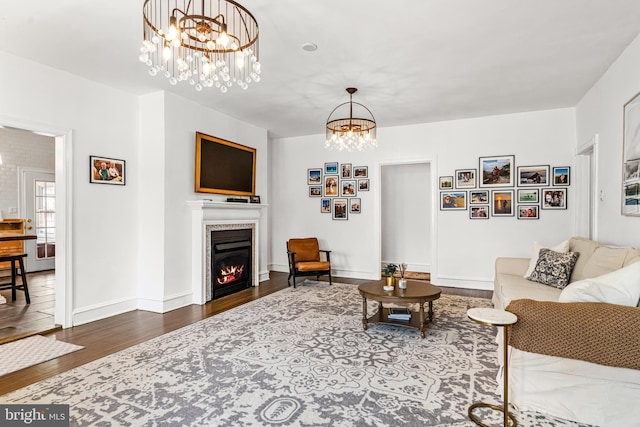 living area featuring a warm lit fireplace, baseboards, a notable chandelier, and wood finished floors