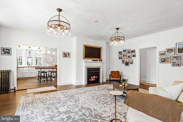 living area featuring baseboards, radiator, wood finished floors, an inviting chandelier, and a lit fireplace