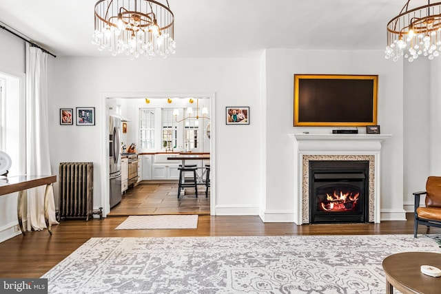 living room with dark wood finished floors, baseboards, radiator heating unit, a glass covered fireplace, and an inviting chandelier