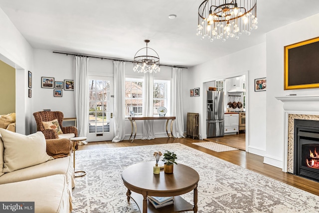 living room featuring an inviting chandelier, a fireplace, baseboards, and wood finished floors