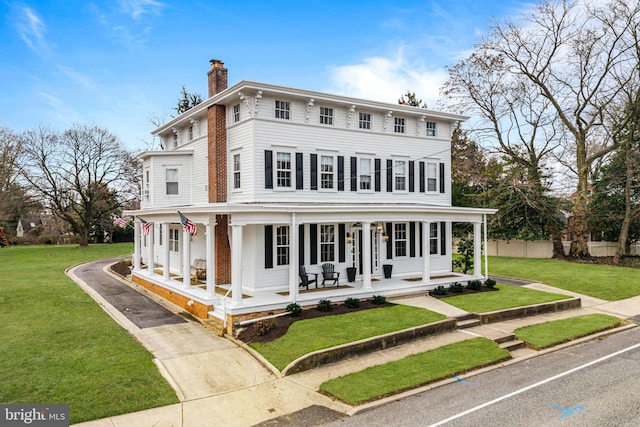 italianate home featuring a porch, a chimney, a front lawn, and fence