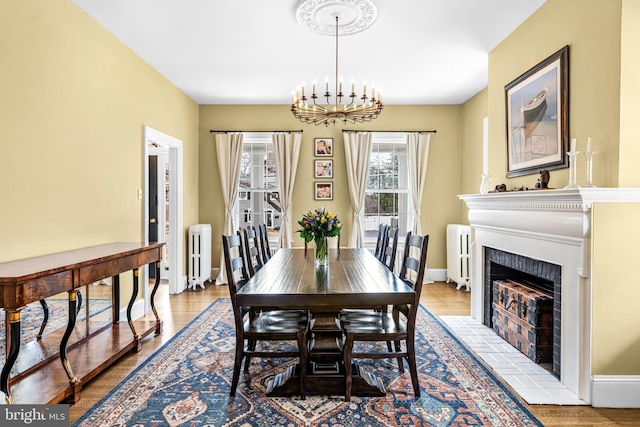 dining space with a chandelier, wood finished floors, radiator heating unit, and a fireplace with flush hearth