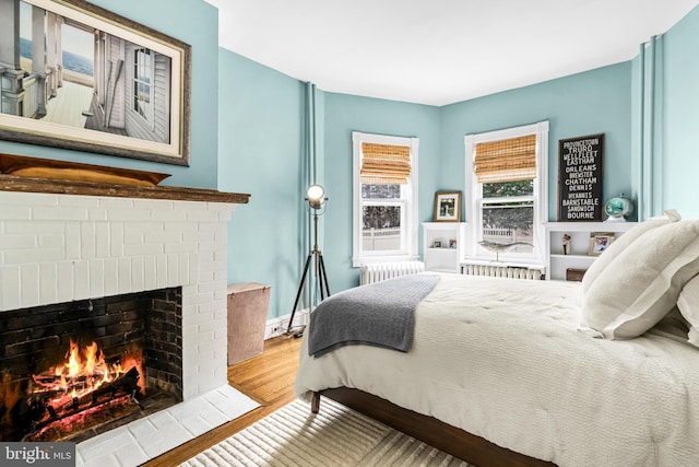 bedroom featuring radiator heating unit, a fireplace, and wood finished floors