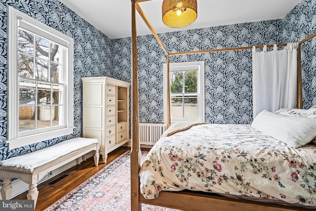 bedroom featuring radiator, wood finished floors, visible vents, and wallpapered walls