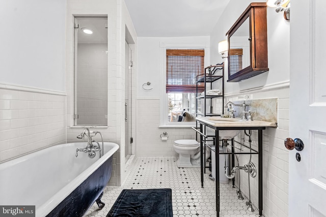 full bath featuring tile walls, toilet, a wainscoted wall, a freestanding tub, and a sink