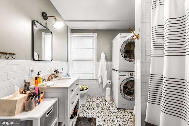 laundry room featuring a wainscoted wall, laundry area, a sink, tile walls, and stacked washer / drying machine