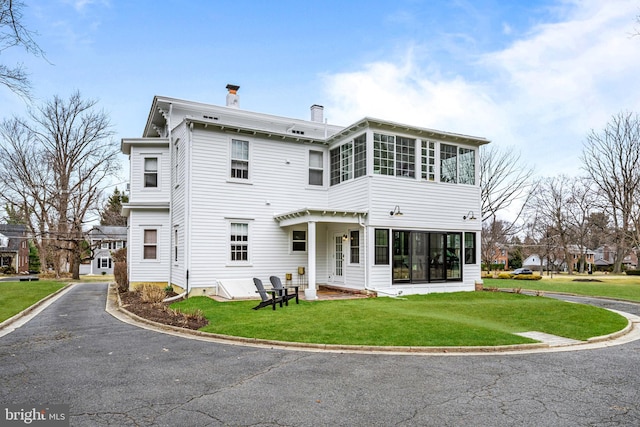 rear view of property with a lawn, a chimney, and a sunroom