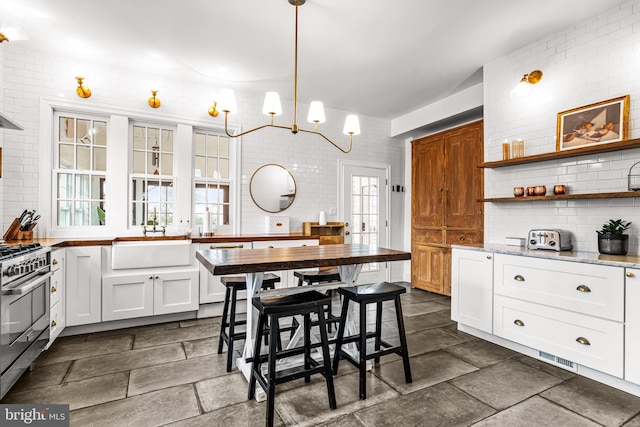 kitchen featuring backsplash, white cabinets, stainless steel range with gas stovetop, a sink, and dishwashing machine