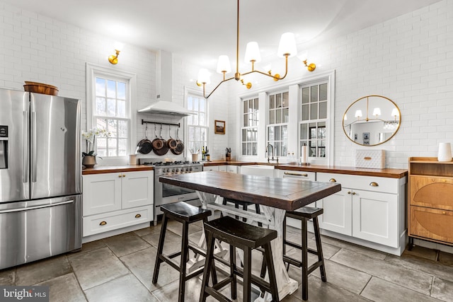 kitchen with wall chimney range hood, white cabinetry, appliances with stainless steel finishes, and wooden counters