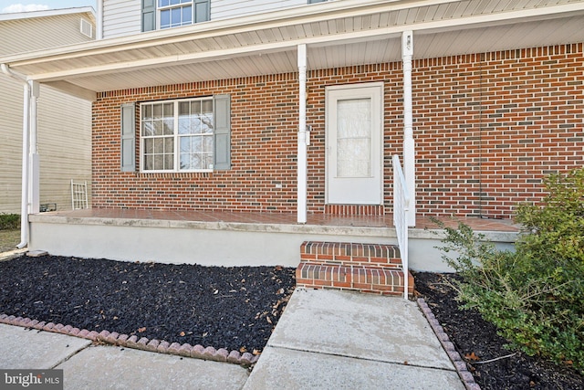 doorway to property with a porch and brick siding