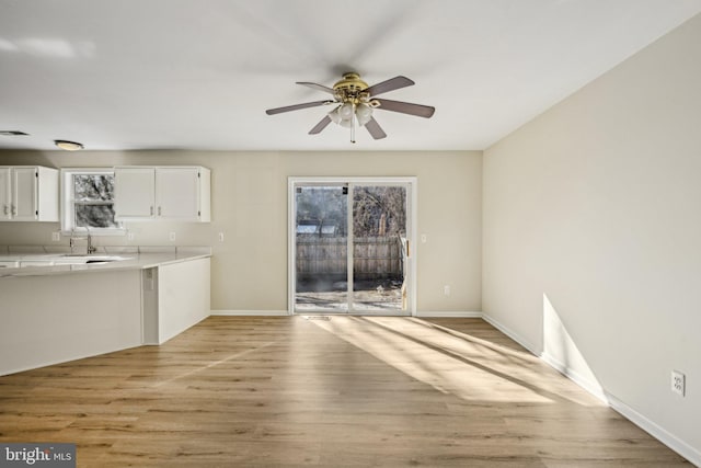 unfurnished living room with light wood finished floors, baseboards, ceiling fan, and a sink