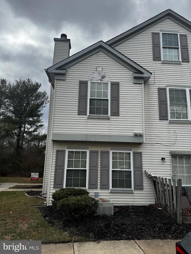 view of front of home featuring a chimney, central AC, and fence