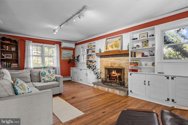 living area featuring a baseboard radiator, wood finished floors, crown molding, a stone fireplace, and a wall mounted AC