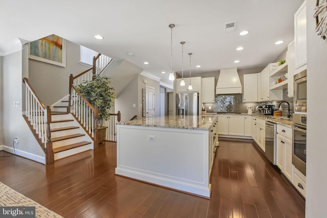 kitchen featuring visible vents, a kitchen island, custom exhaust hood, stainless steel appliances, and a sink