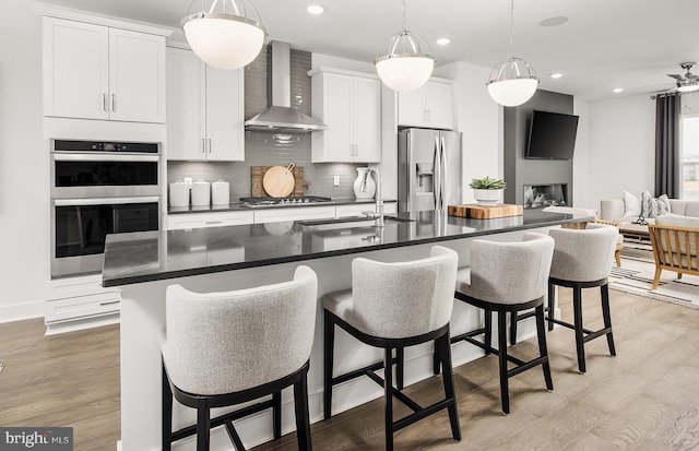 kitchen with decorative backsplash, dark countertops, wall chimney exhaust hood, appliances with stainless steel finishes, and a sink