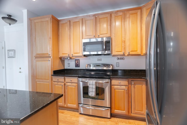 kitchen featuring ornamental molding, light brown cabinets, dark stone countertops, light wood-style floors, and appliances with stainless steel finishes