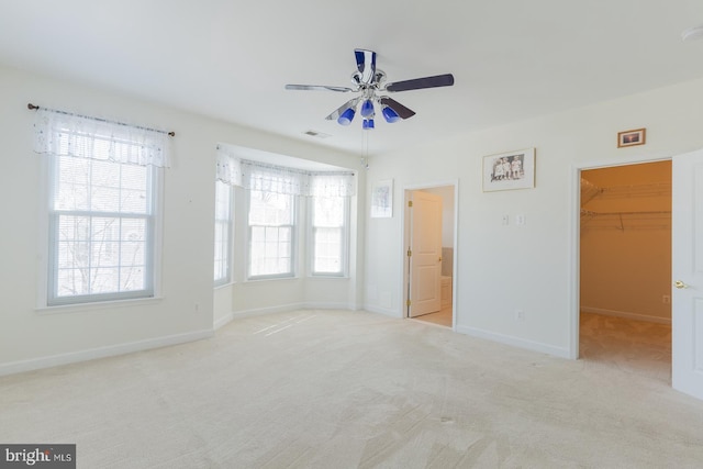 unfurnished bedroom with carpet, visible vents, baseboards, ceiling fan, and a walk in closet