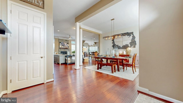 dining space with baseboards, a stone fireplace, wood finished floors, and a ceiling fan