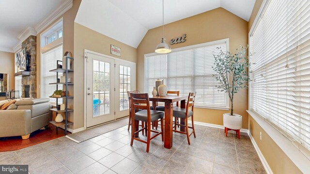 dining area featuring light tile patterned floors, baseboards, a stone fireplace, and vaulted ceiling