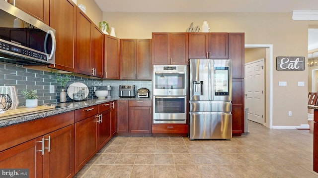 kitchen featuring dark stone countertops, backsplash, appliances with stainless steel finishes, light tile patterned floors, and baseboards