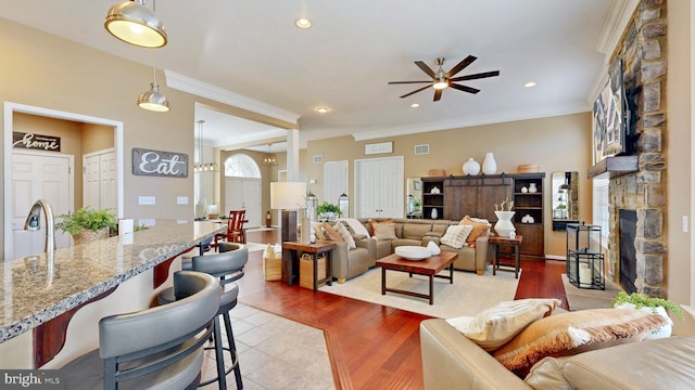 living area with light wood finished floors, visible vents, crown molding, a stone fireplace, and recessed lighting