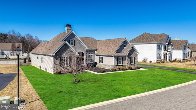 view of front of house with stone siding, a front yard, roof with shingles, and a chimney