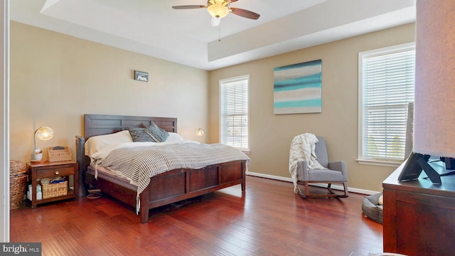 bedroom with ceiling fan, a tray ceiling, baseboards, and dark wood-style floors