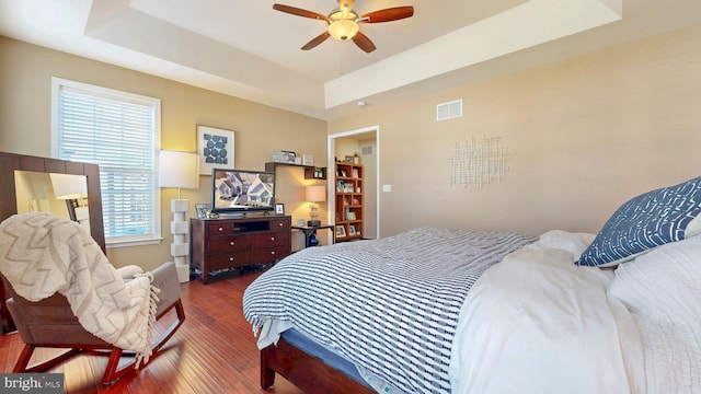 bedroom with visible vents, a ceiling fan, dark wood-type flooring, and a tray ceiling