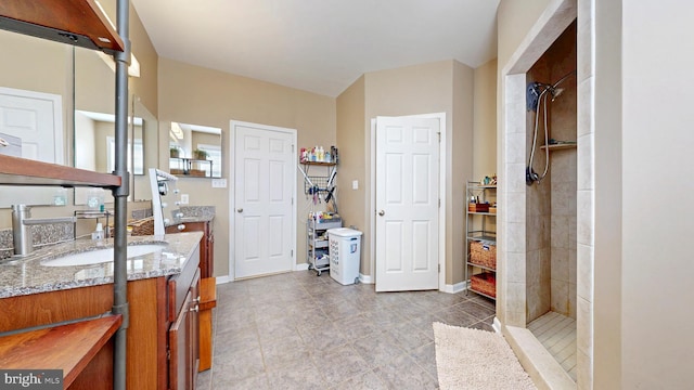 bathroom with baseboards, tiled shower, and vanity