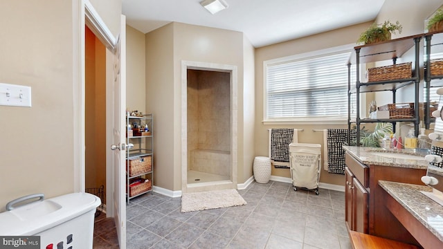 bathroom featuring tile patterned flooring, baseboards, vanity, and a tile shower