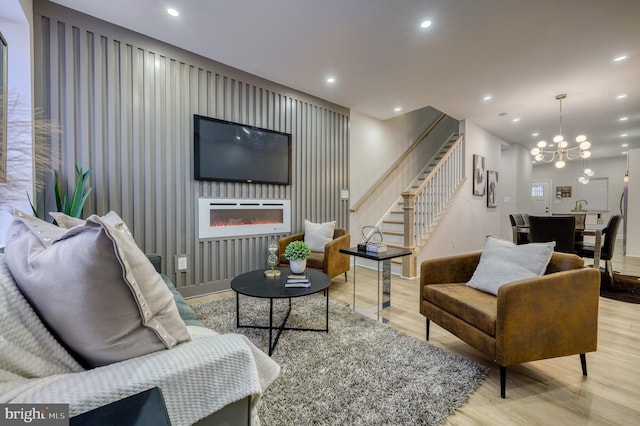 living area featuring wood finished floors, recessed lighting, stairs, a glass covered fireplace, and a chandelier