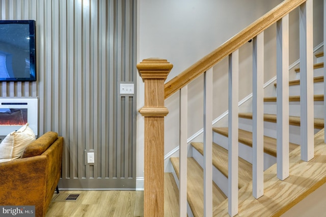 stairway featuring a glass covered fireplace, visible vents, wood finished floors, and wallpapered walls