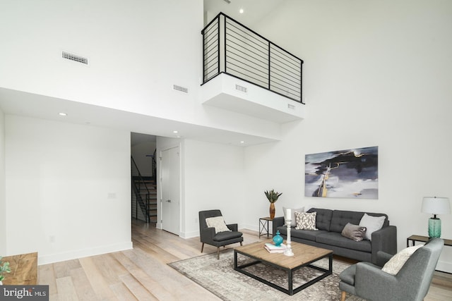 living room featuring stairway, a high ceiling, visible vents, and wood finished floors