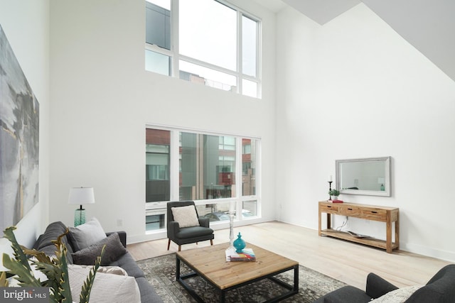 living area with a towering ceiling, baseboards, and wood finished floors