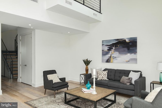 living room with wood finished floors, a towering ceiling, visible vents, stairs, and baseboards