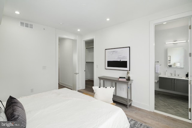 bedroom with visible vents, light wood-style flooring, a walk in closet, a sink, and recessed lighting