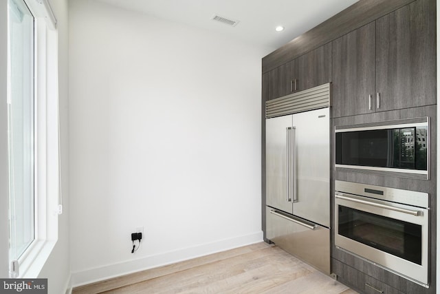 kitchen with built in appliances, visible vents, baseboards, dark brown cabinets, and light wood finished floors