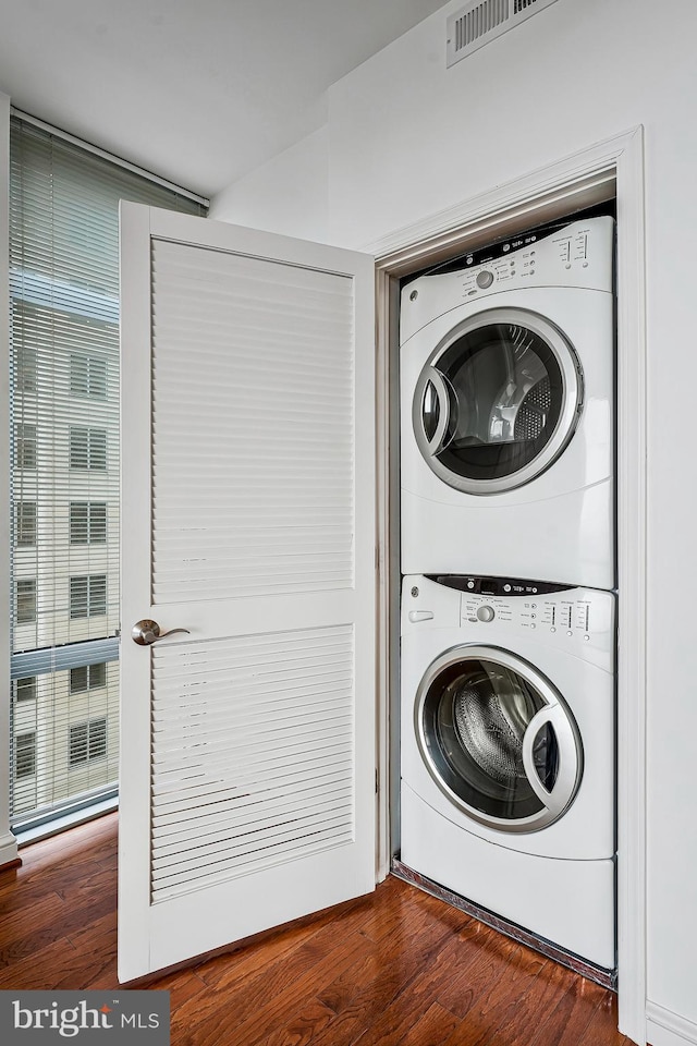 clothes washing area featuring laundry area, visible vents, stacked washer / drying machine, and dark wood-type flooring