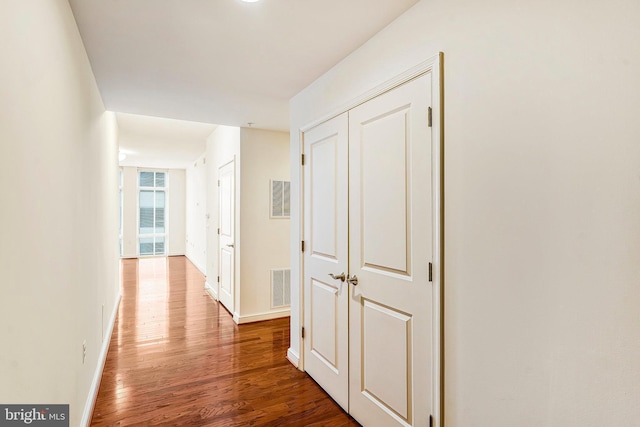 corridor featuring visible vents, baseboards, and wood finished floors