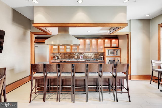 kitchen featuring a kitchen breakfast bar, built in appliances, backsplash, and island range hood