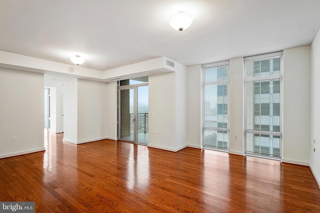 spare room with visible vents, floor to ceiling windows, baseboards, and wood finished floors