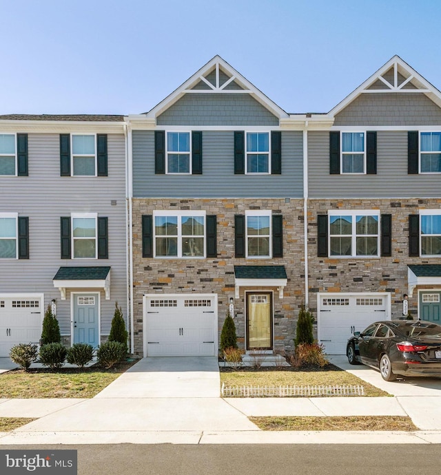 townhome / multi-family property with stone siding, driveway, and an attached garage