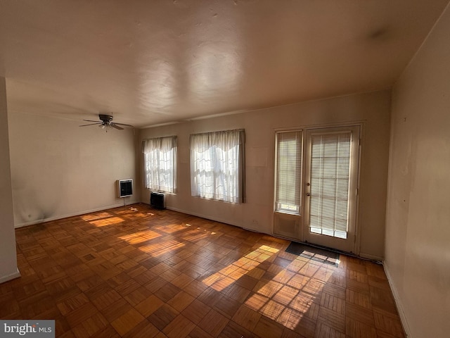 empty room featuring baseboards, a ceiling fan, and heating unit