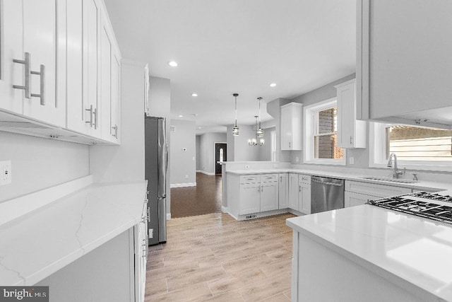 kitchen with decorative light fixtures, stainless steel appliances, white cabinetry, a sink, and a peninsula